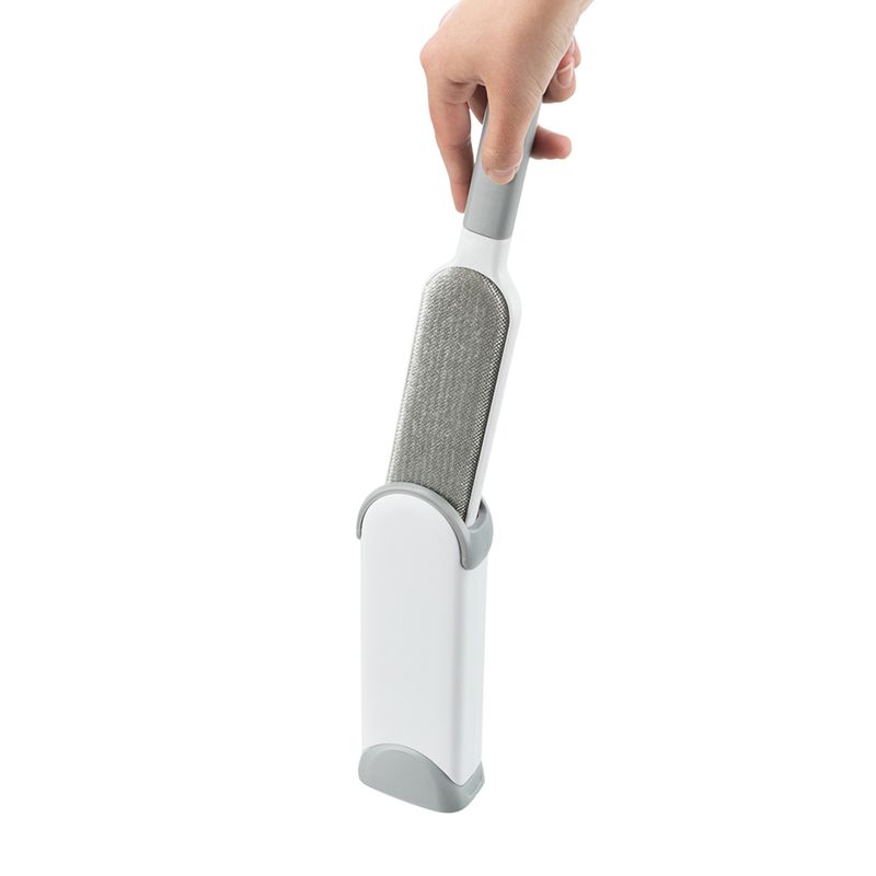 Hand holding a grey and white lint brush with self-cleaning base, suitable for removing pet hair.