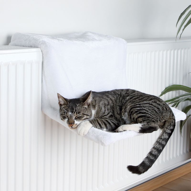 Cat bed made of white fabric, attached to a radiator. A grey cat is lying relaxed on it.