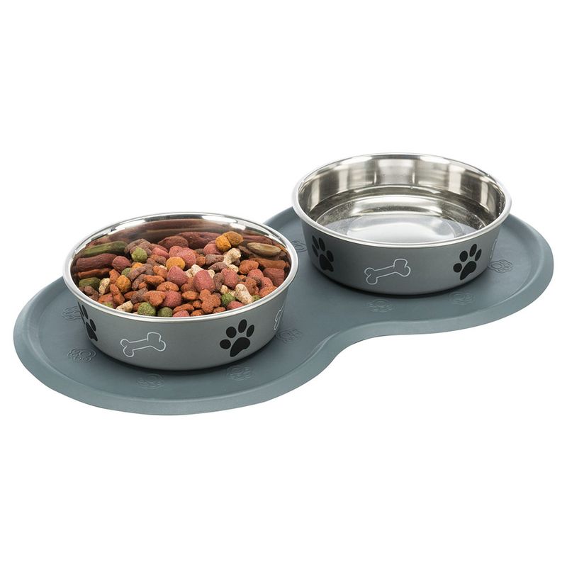 Double bowl set with grey mat, two stainless steel bowls: one filled with dry food, the other empty. Design with paw and bone motifs.