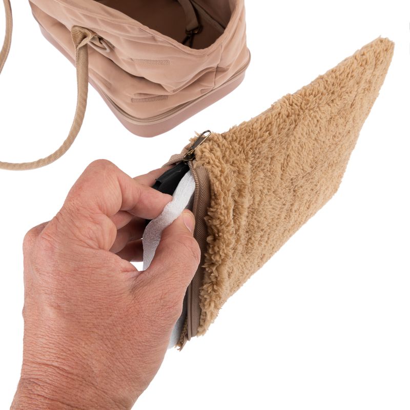 Hand showing removable inner padding from a beige bag with zip and plush material.