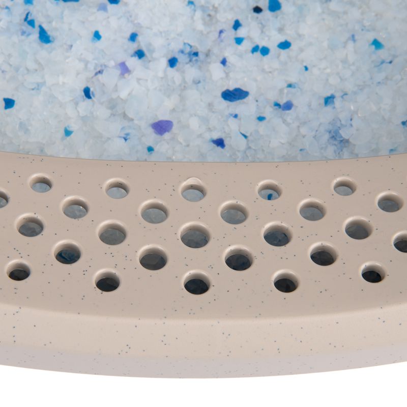 Close-up of cat litter with blue and white crystals and a beige perforated plastic tray.