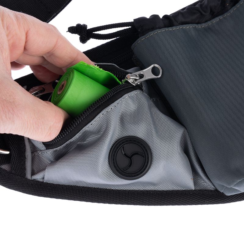 Hand removes green dog waste bag roll from grey bag with zip and dispenser opening.