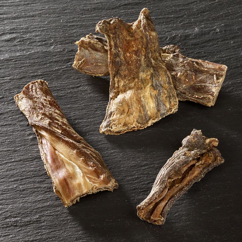 Four pieces of dried, natural meat chews displayed on a dark surface, showing their texture and size for product comparison.