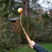 Throwing arm made of orange plastic with a yellow-orange ball, suitable for throwing balls outdoors.