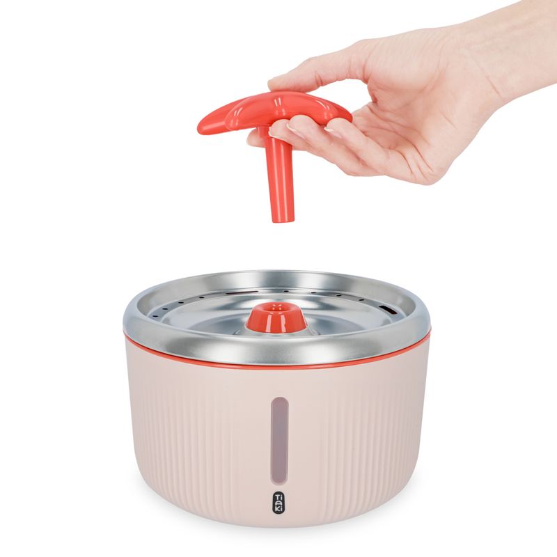 Hand showing the installation of a red spare part on a drinking fountain with stainless steel surface and water level indicator.