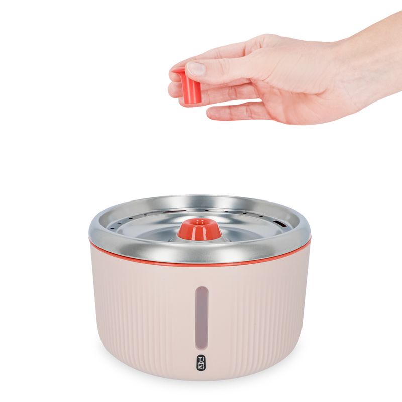 Hand holding a red filter insert for a drinking fountain with stainless steel surface and water level indicator.