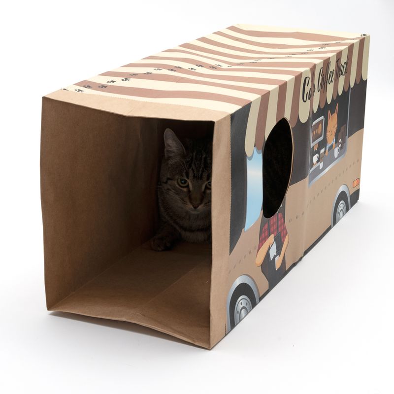 Cardboard cat playhouse shaped like a coffee truck with striped roof and round opening, cat sitting inside.