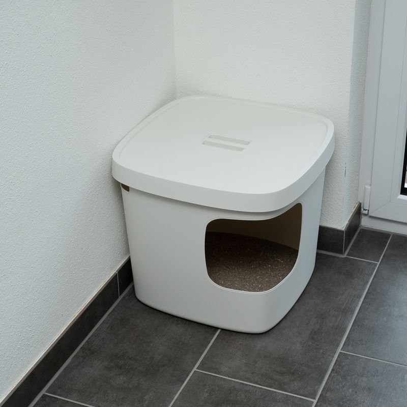 Corner cat litter box with white lid and side entrance, placed on grey tiles.