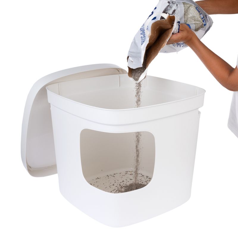 Person pouring cat litter from a package into a white cat toilet with removable lid.