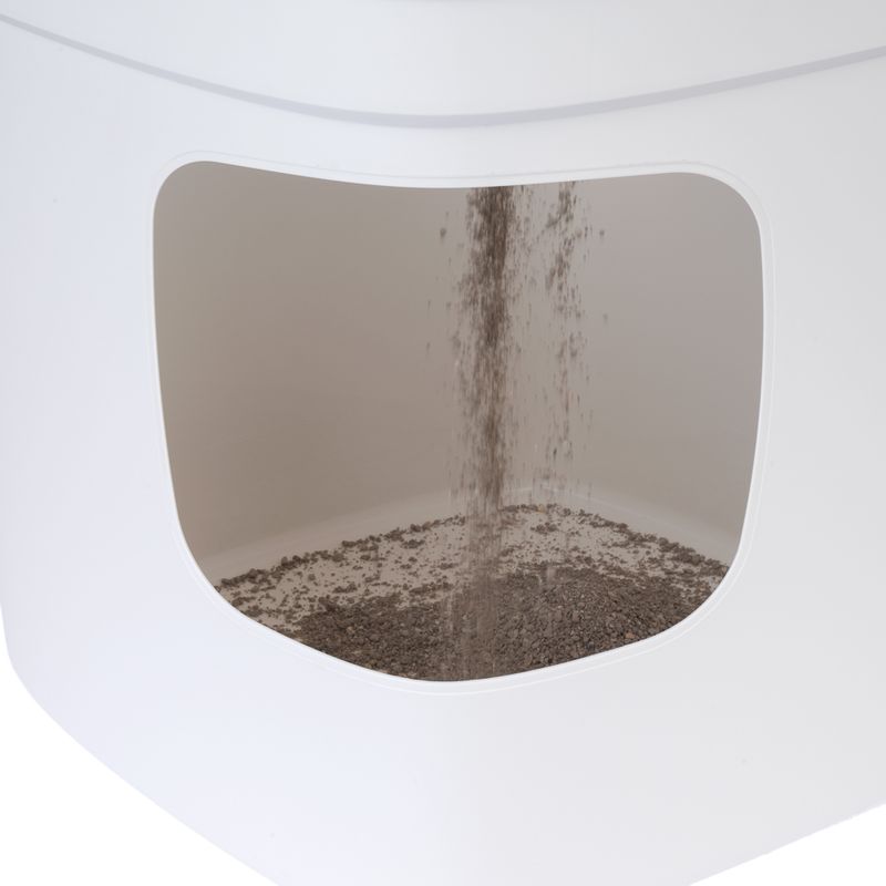 Close-up of a white container with litter falling through an opening and collecting at the bottom.