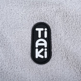 Tiaki. Brand logo on grey fabric background.