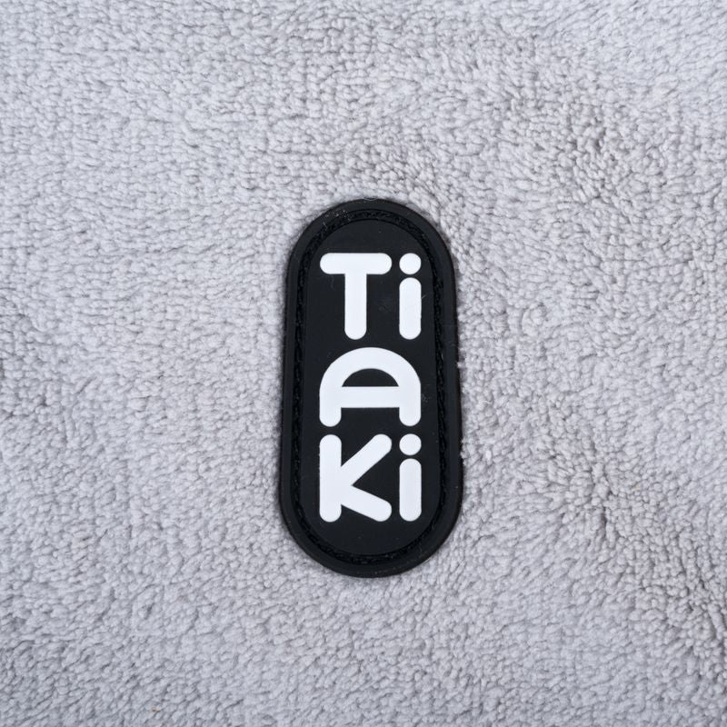 Tiaki. Brand logo on grey fabric background.