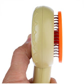 Hand holding a beige brush with an orange head and metal bristles, suitable for coat care.