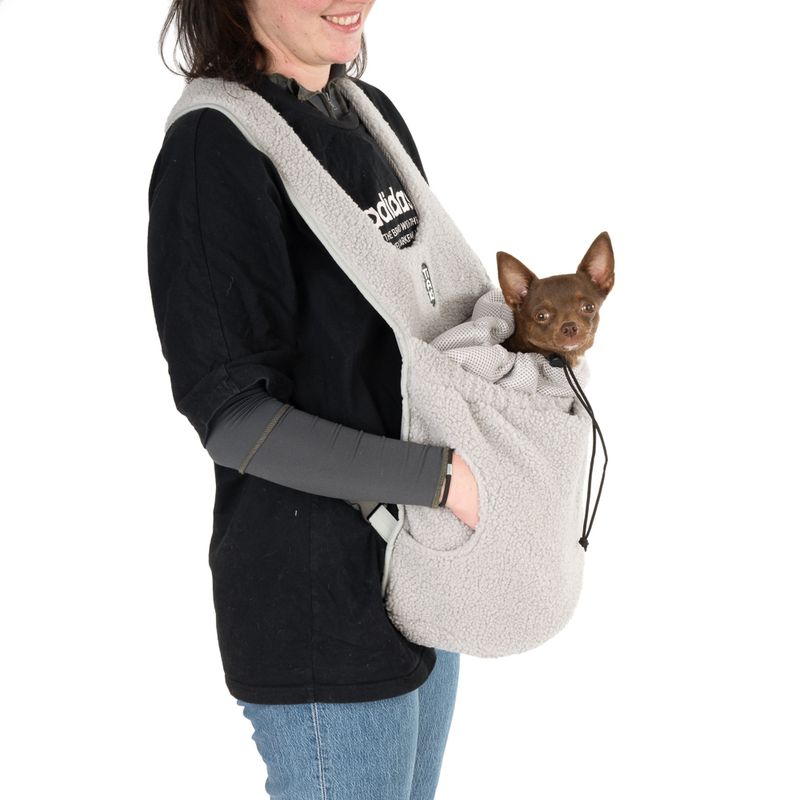 Person carrying a grey fleece carrier bag with a small dog inside. Bag has adjustable straps and drawstring.