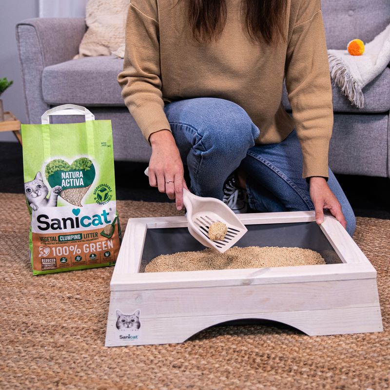Sanicat Natura Active cat litter, 100% green, plant-based clumping. Woman demonstrates use with litter scoop in cat toilet.