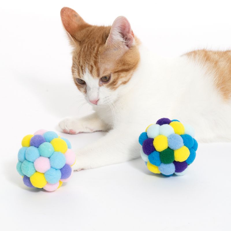 Cat toy: two colourful balls made of soft fabric pom-poms, cat interacting with one ball.