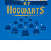 Hogwarts lettering in gold with illustration of boats on water heading to the castle.
