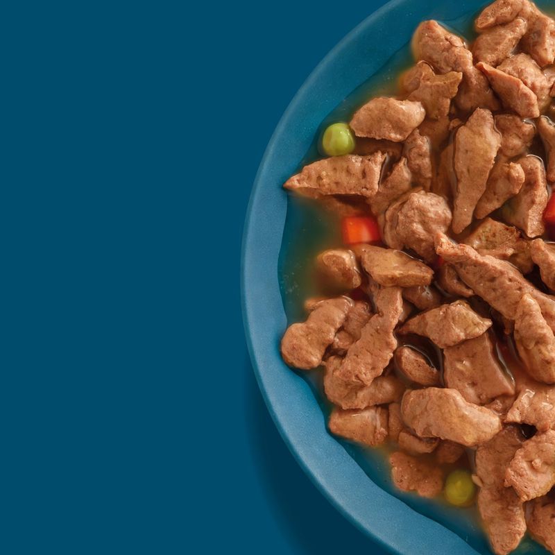 Tray with meat pieces in gravy, with visible peas and carrot pieces.