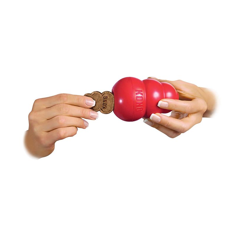 Red KONG toy ball filled with a KONG treat, shown held by two hands.