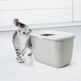 Cat litter box with top entry, grey design, next to a grey and white striped cat. Suitable for modern interiors.