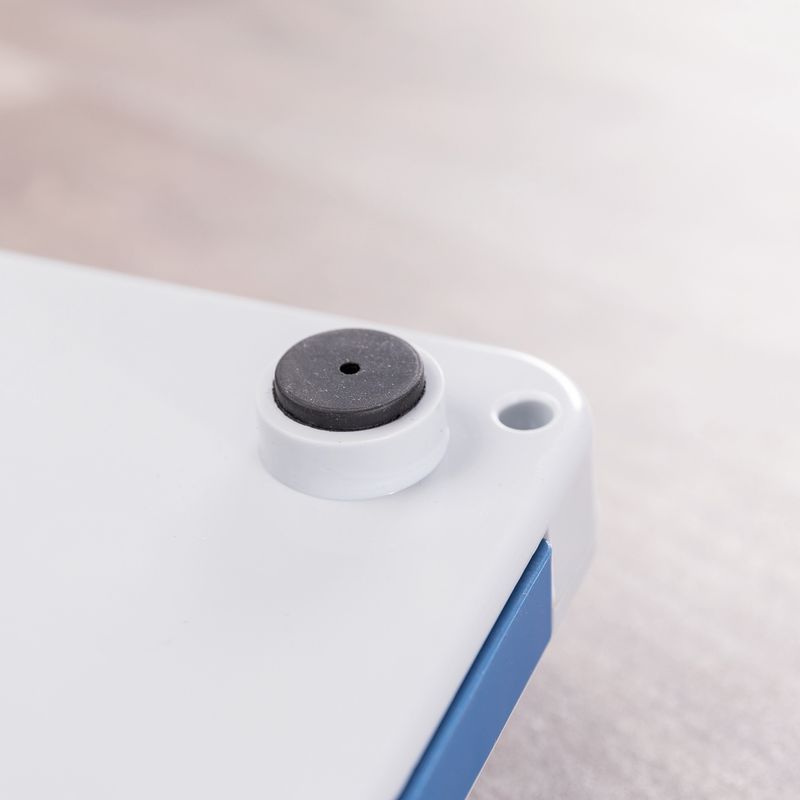 Close-up of a white plastic surface with a black round rubber foot and a small opening at the corner.
