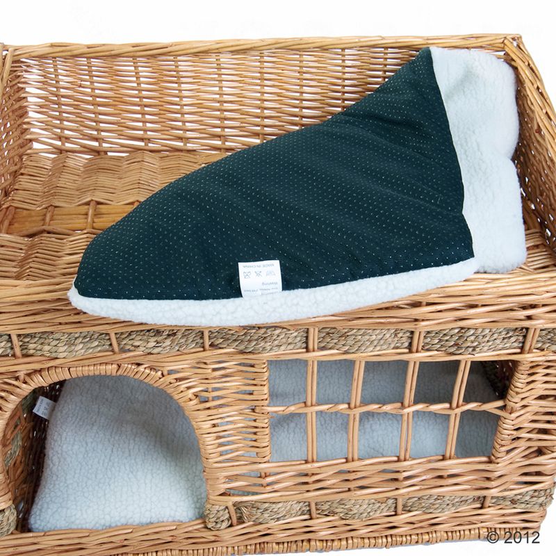 Wicker basket with removable dark green cushion and white fleece underside. Care instructions visible on label: washable at 30°C, do not bleach.