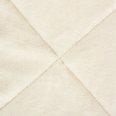 Close-up of a cream-coloured, soft fabric with diagonal seams. Material texture visible.