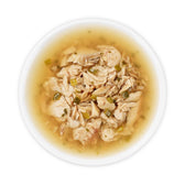 Close-up of a bowl with shredded chicken in broth, garnished with green vegetable pieces.