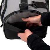 Close-up of a black bag with grey accents. Hands open a front zip pocket that provides additional storage space.