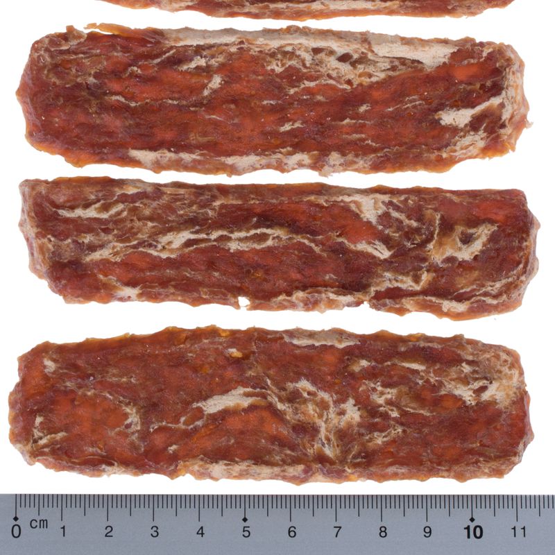Four elongated dog snacks with brown and white marbling, arranged side by side. Scale at the bottom shows length of approx. 10 cm.