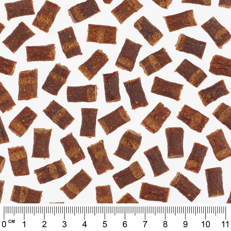 Close-up of brown snack pieces with ruler for size reference, pieces approximately 2-3 cm long.